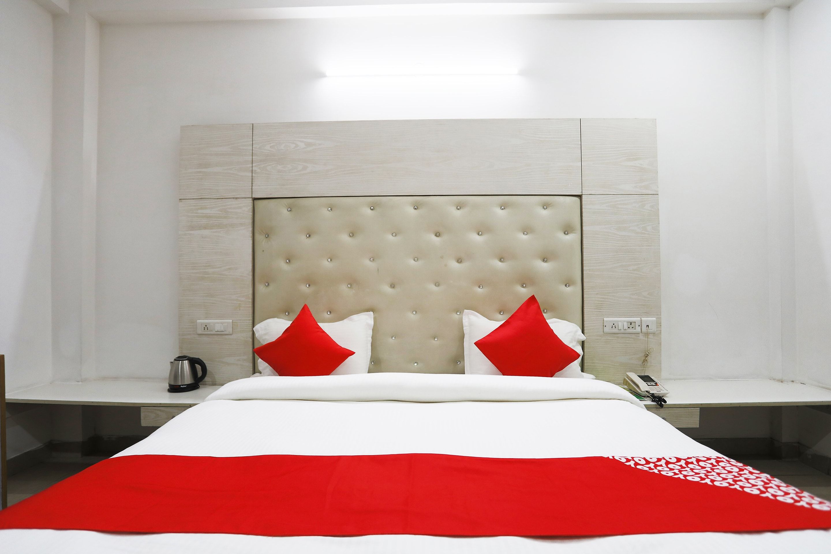 A hotel room with a large bed, two bedside tables, a red and white bedspread, and a modern headboard.