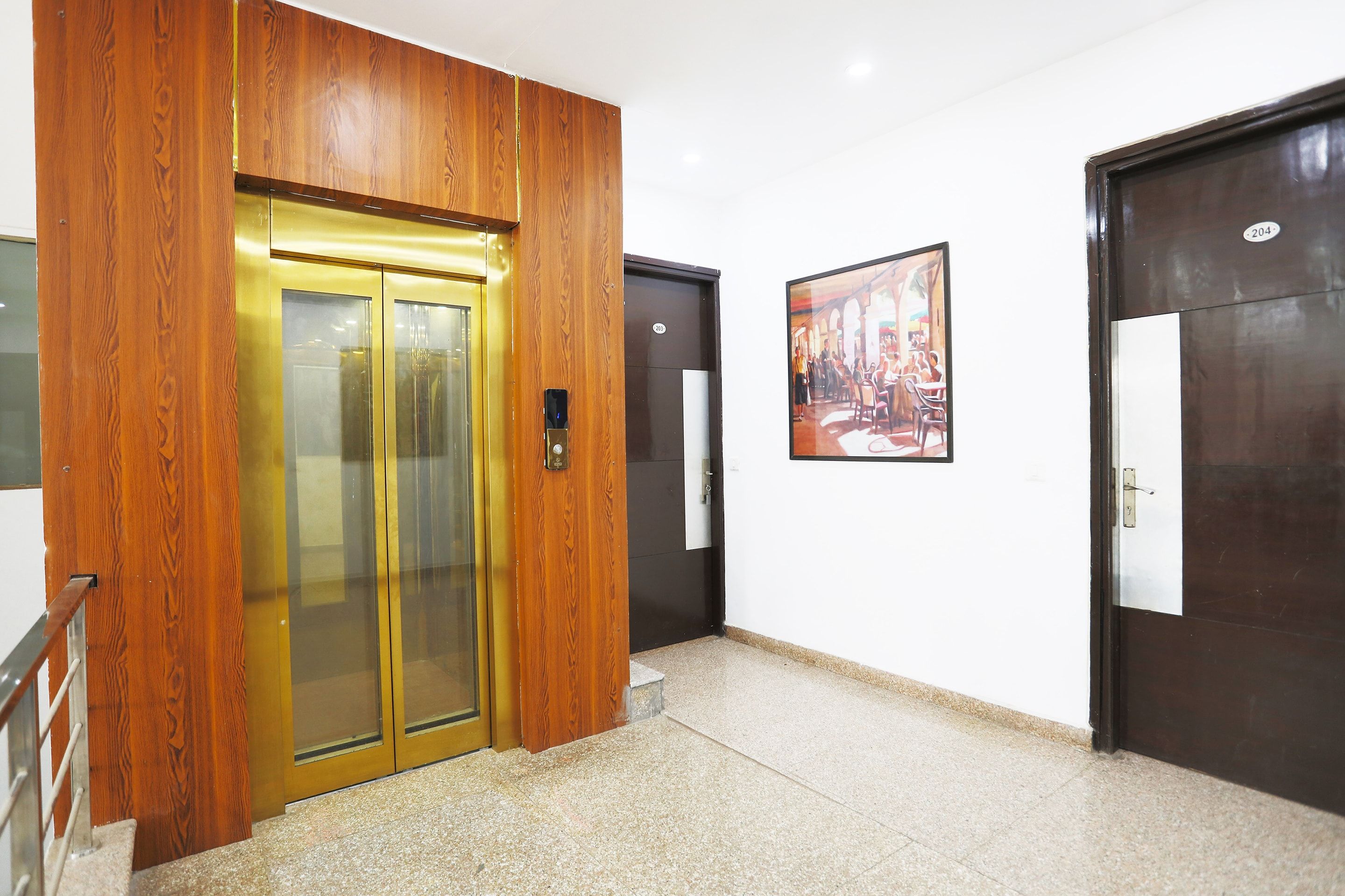 A hallway with a wooden elevator, a door with a number plate, and a framed picture on the wall.