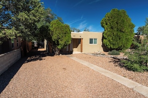 A residential property with a gravel driveway, a small building with a window, and surrounding trees.