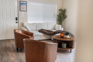 A living room with a white sofa, two brown armchairs, a round coffee table with decorative items, and a large window with blinds. - 3-bedroom house in tranquil Albuquerque Home away from Home (Albuquerque)