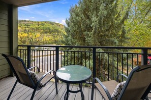 A balcony with a glass table and two chairs, overlooking a forested hillside. - Spacious Vail Condo, steps to Free Shuttle | BW534 (Vail)