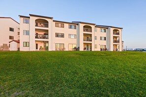 Edifício residencial com vários andares, varandas, telhado plano e um gramado bem cuidado.