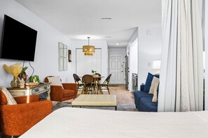 A modern living room with a flat-screen TV, a dining area with a table and chairs, and a separate seating area with a sofa and a bed. - 🏖️Cozy Sound-Front Studio | Community Pool + Pier | Sunset Harbor Palms 1-204 (Navarre)