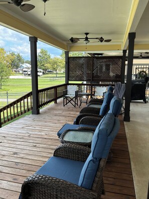 A covered outdoor seating area with wicker chairs and a table, overlooking a grassy field. - Waterfront, 4 bedroom house conveniently locate near Lake Livingston State Park (Livingston)