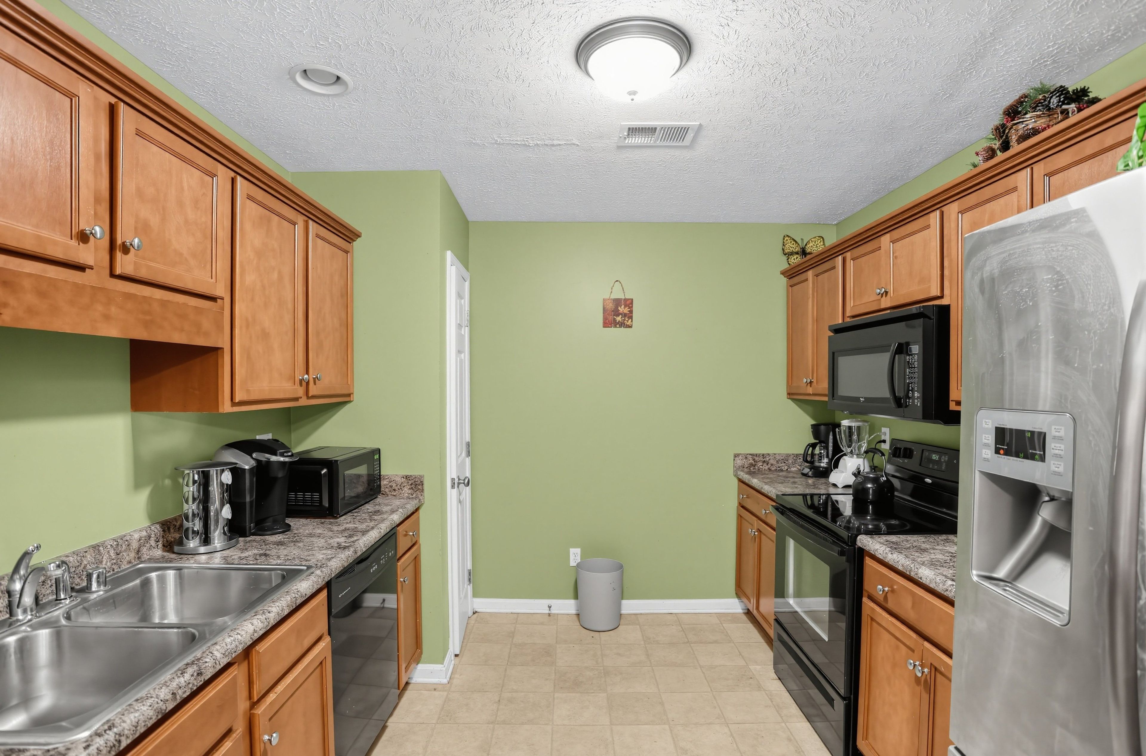 A kitchen with wooden cabinets, a stainless steel refrigerator, a microwave, a stove, and a sink.