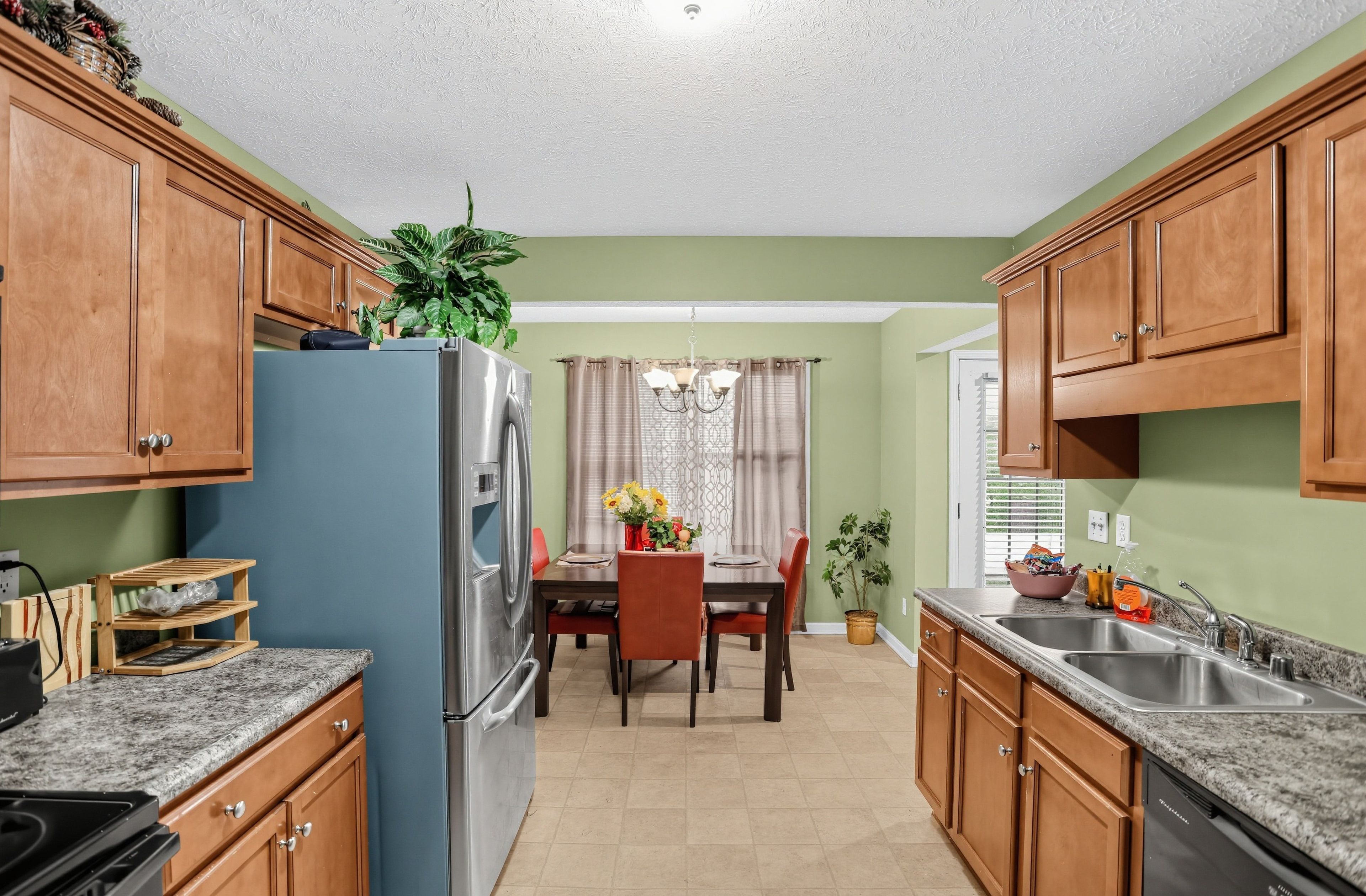 A kitchen with wooden cabinets, a blue refrigerator, a dining table with chairs, and a chandelier.