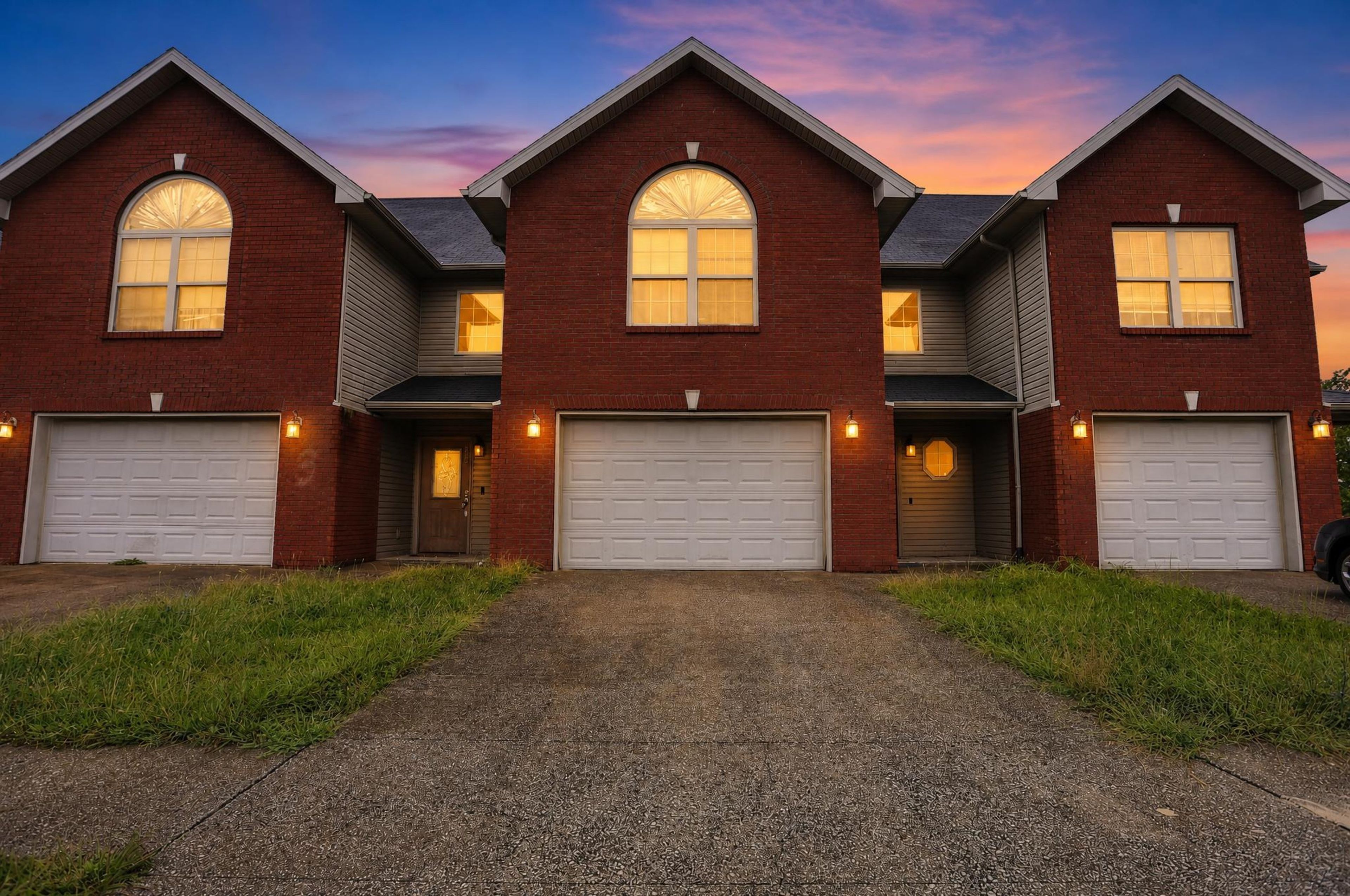 A three-story brick house with a symmetrical design, featuring two garages on each side and a central entrance.