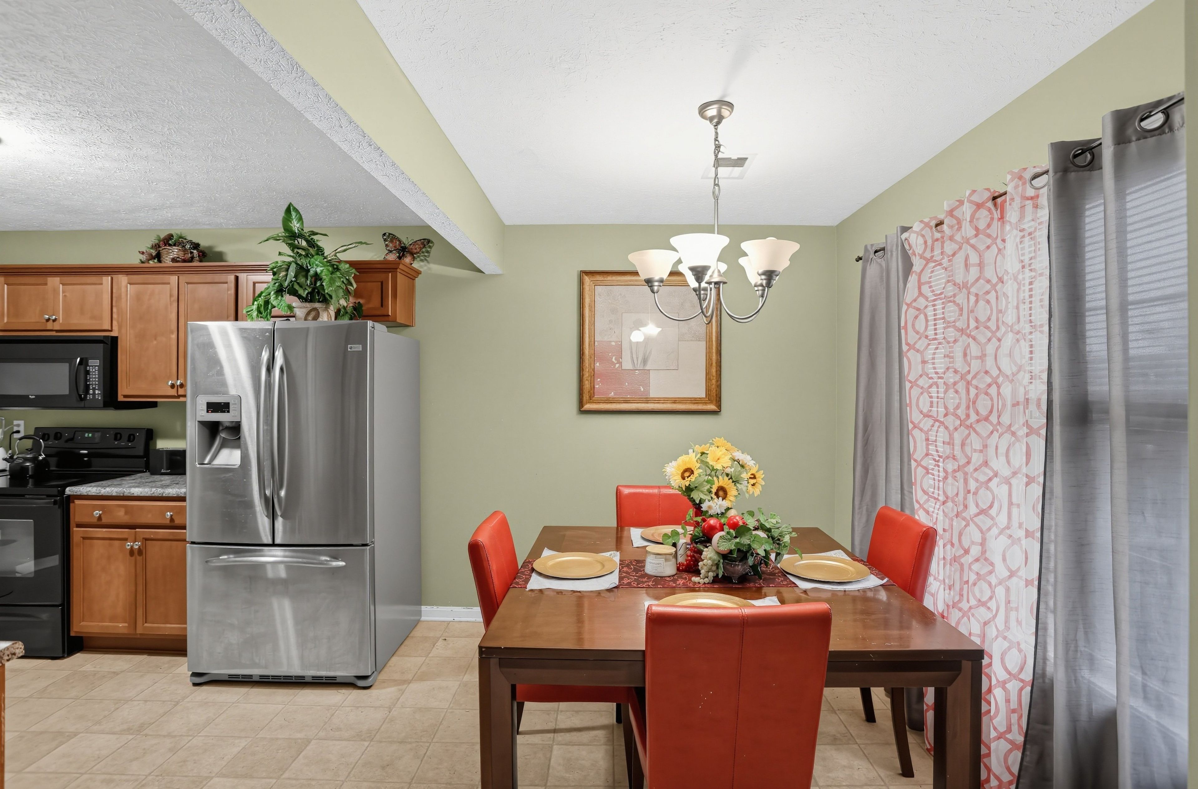 A kitchen with a stainless steel refrigerator, a microwave, and a stove. There is a dining table with chairs and a chandelier above it.