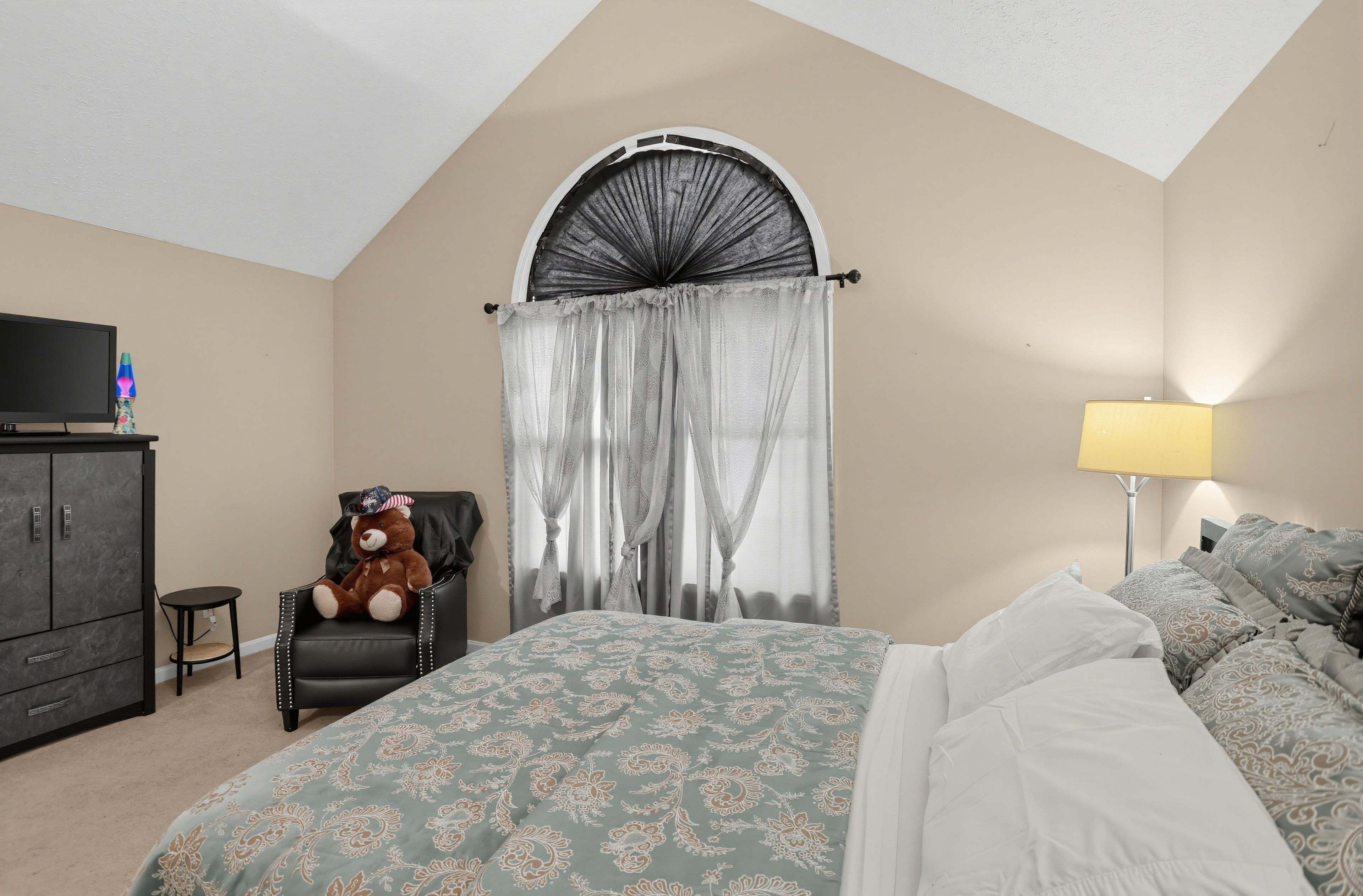 A bedroom with a bed, a chair, a television, a lamp, and a teddy bear.