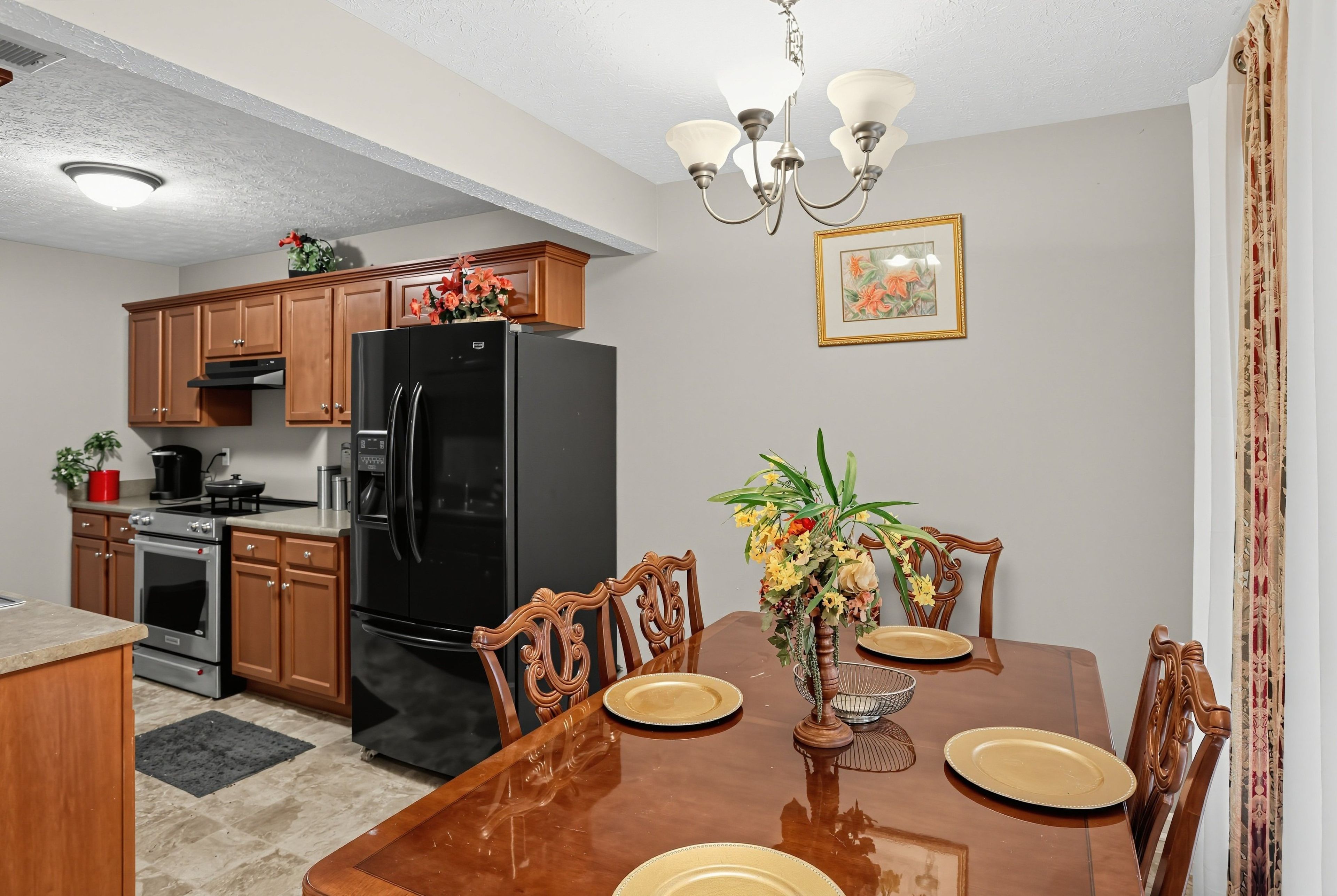 A kitchen with wooden cabinets, a black refrigerator, a dining table with chairs, and a chandelier.