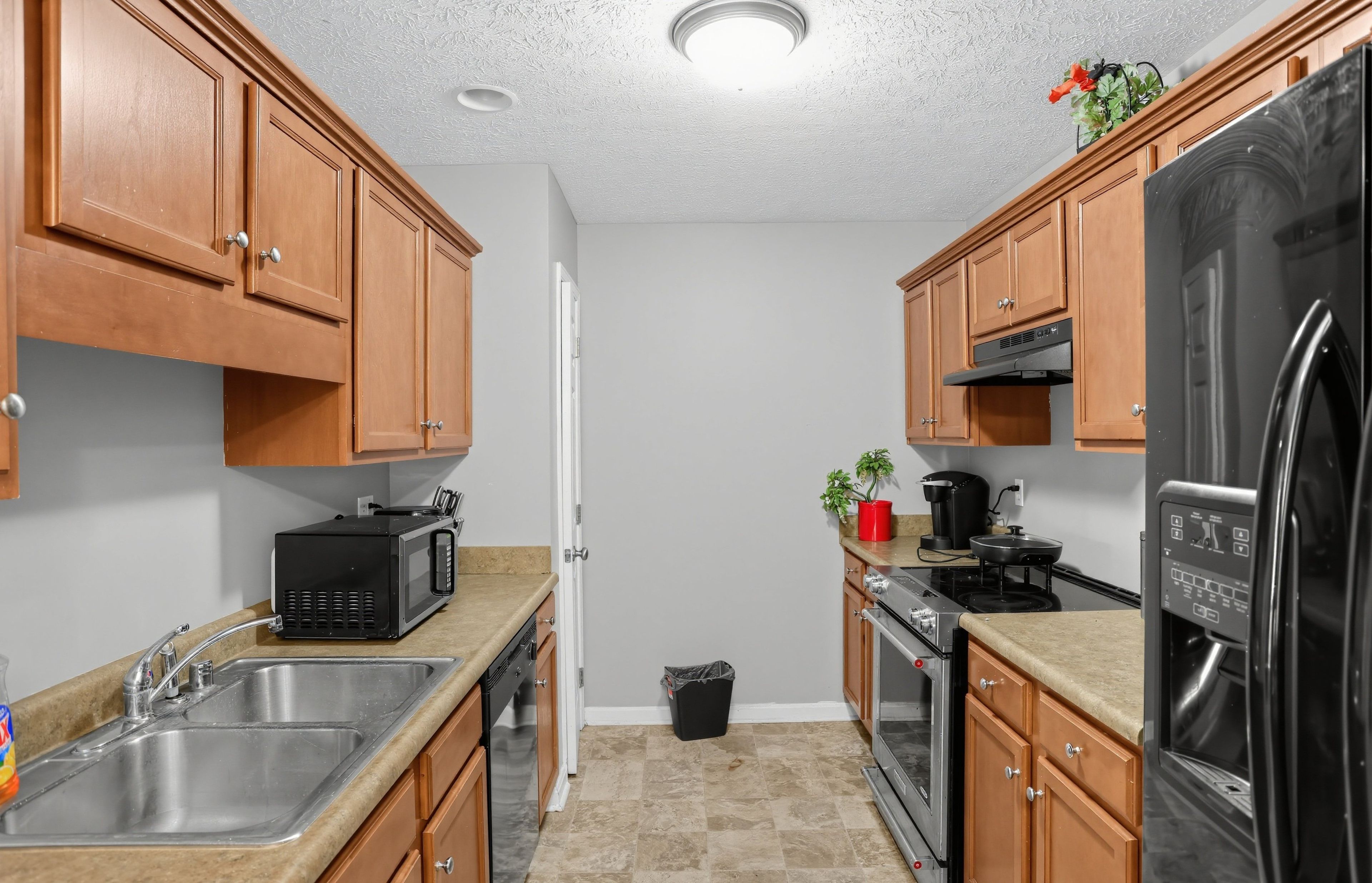 A compact kitchen with wooden cabinets, a stainless steel sink, a microwave, a stove, and a refrigerator.
