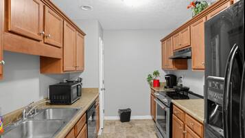 A compact kitchen with wooden cabinets, a stainless steel sink, a microwave, a stove, and a refrigerator.