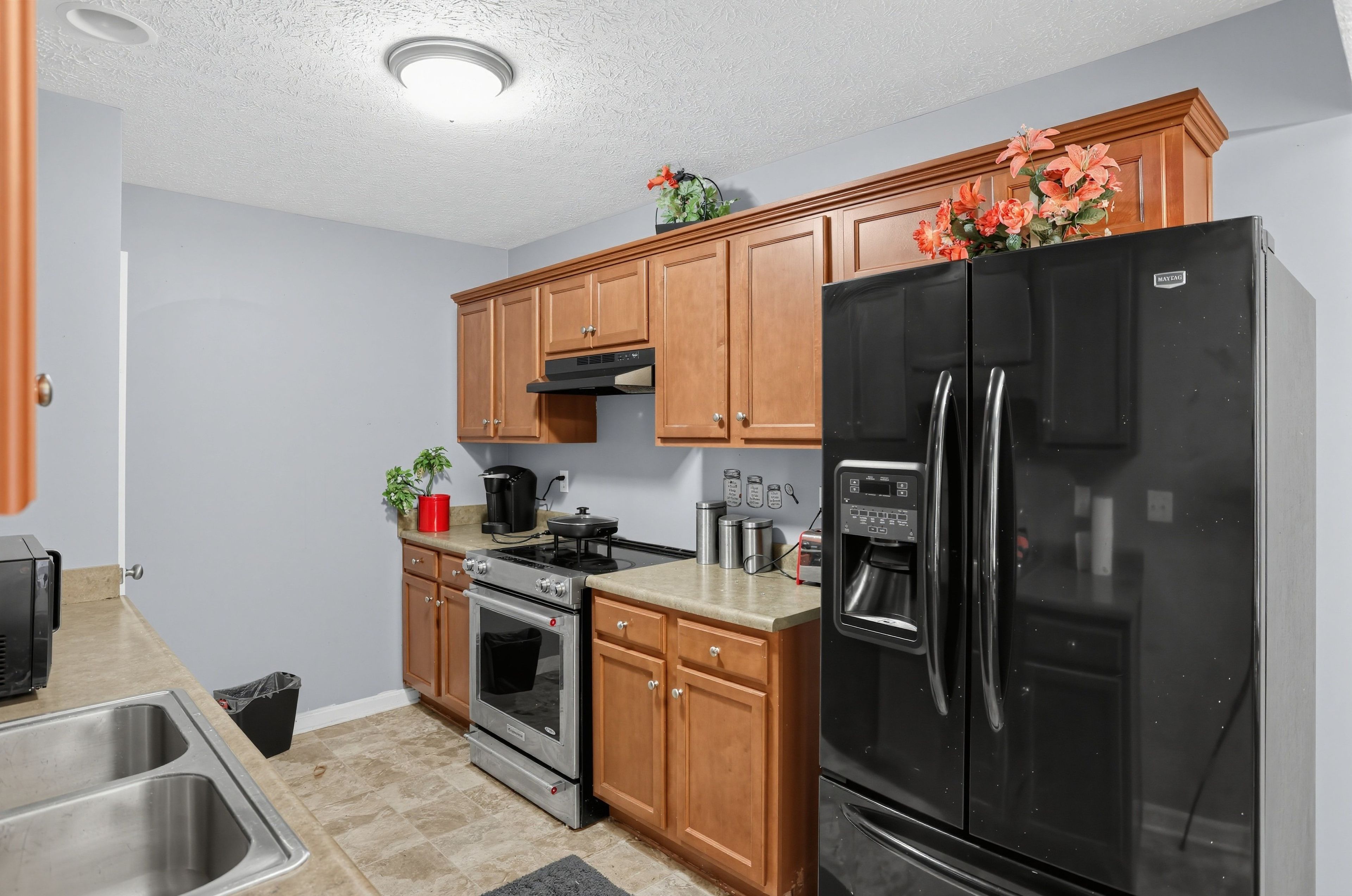 A kitchen with wooden cabinets, a black refrigerator, stainless steel appliances, and a small countertop area.