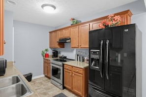 Una cocina con armarios de madera, un refrigerador negro, electrodomésticos de acero inoxidable y una pequeña área de encimera.