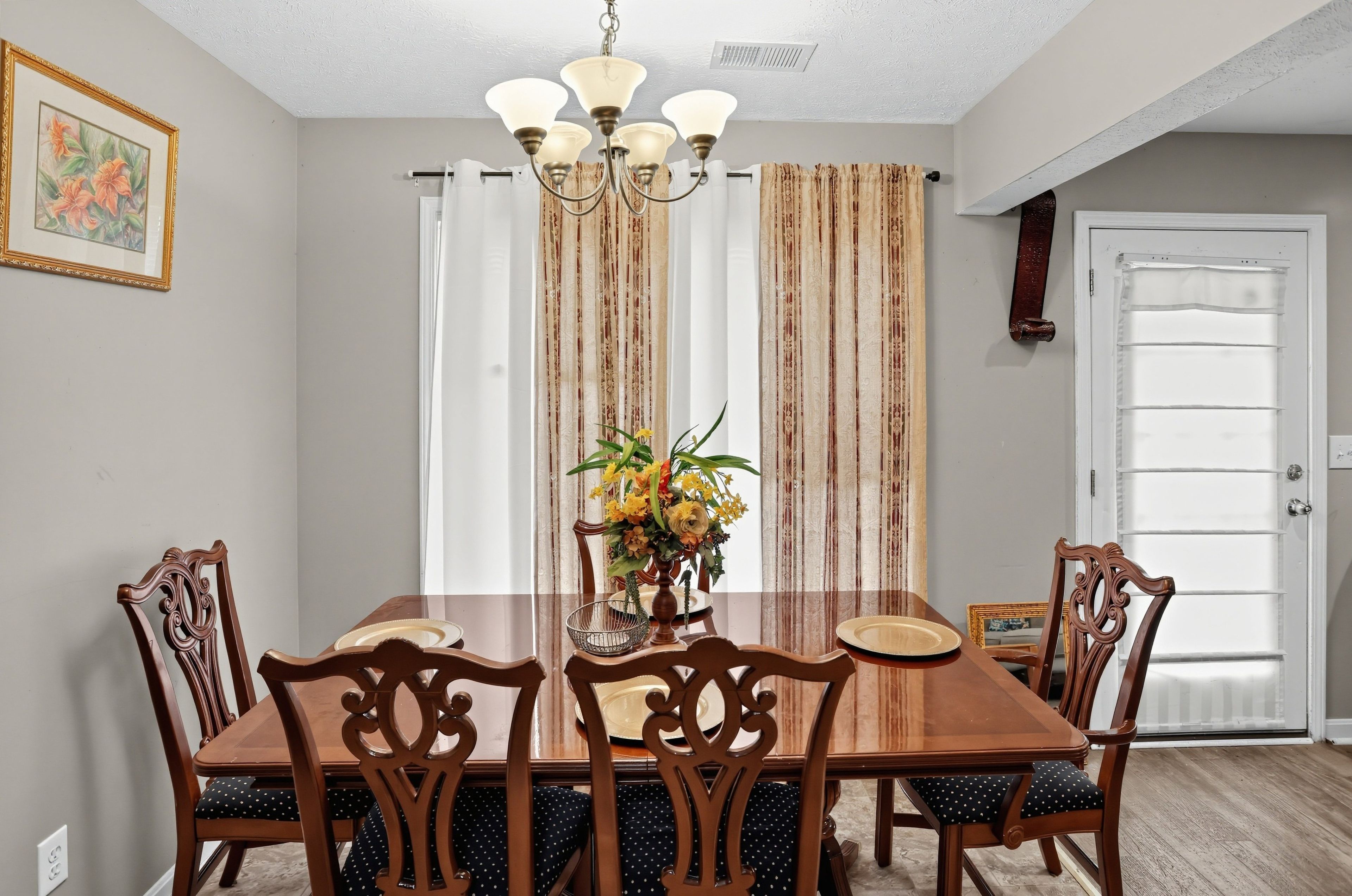 A dining room with a wooden table and chairs, a chandelier, and curtains.