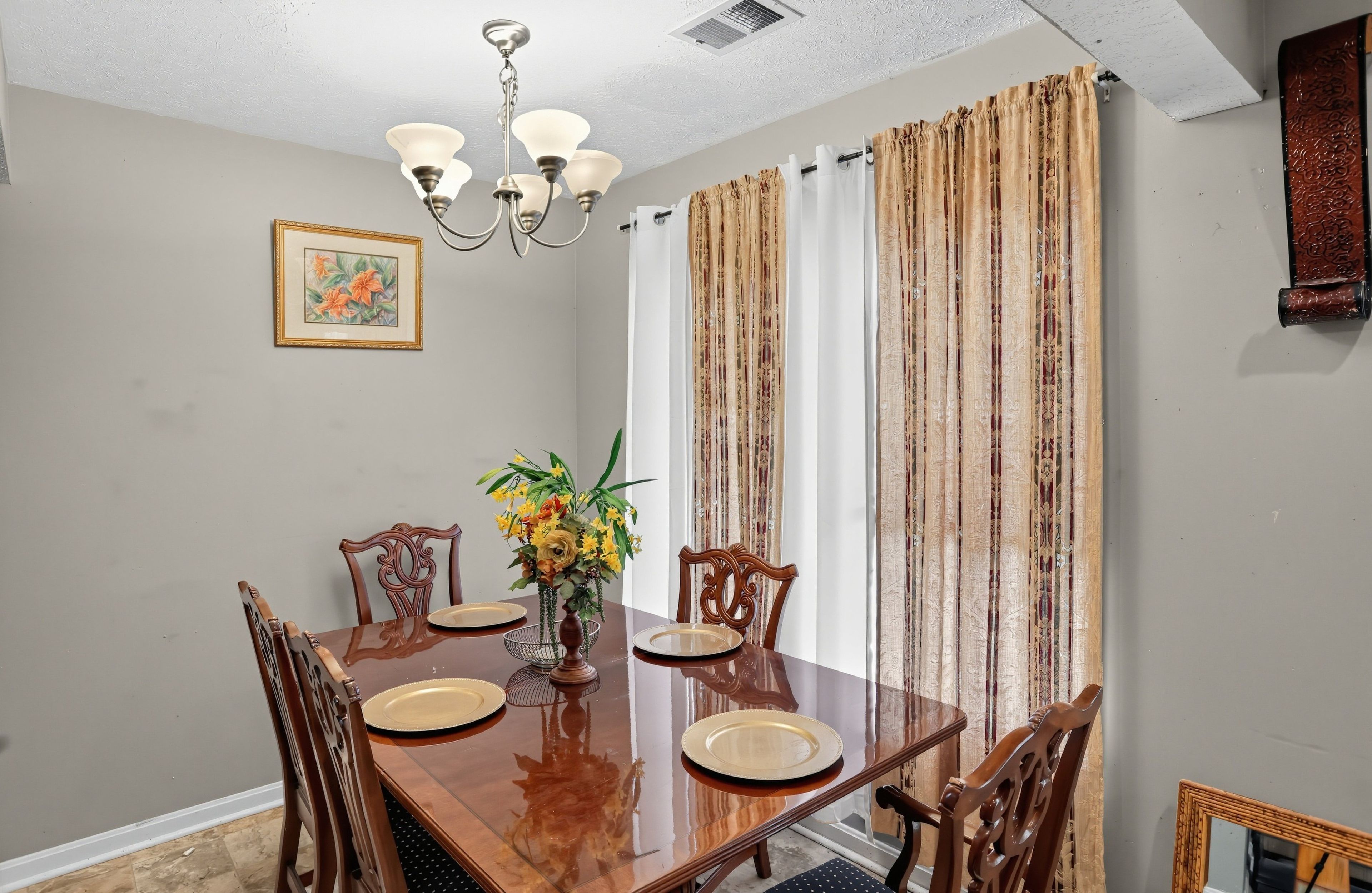 A dining area with a wooden table, chairs, a chandelier, and a floral centerpiece.