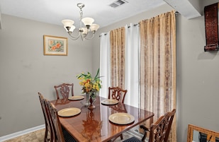 Un comedor con mesa de madera, sillas, una araña y un centro de mesa floral.