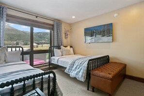 A bedroom with two beds, a bench, a window with a view of a mountain, and a mounted deer head. - 2br Deer Valley Retreat Hot Tub & Fireplace 2 Bedroom Condo (Park City)