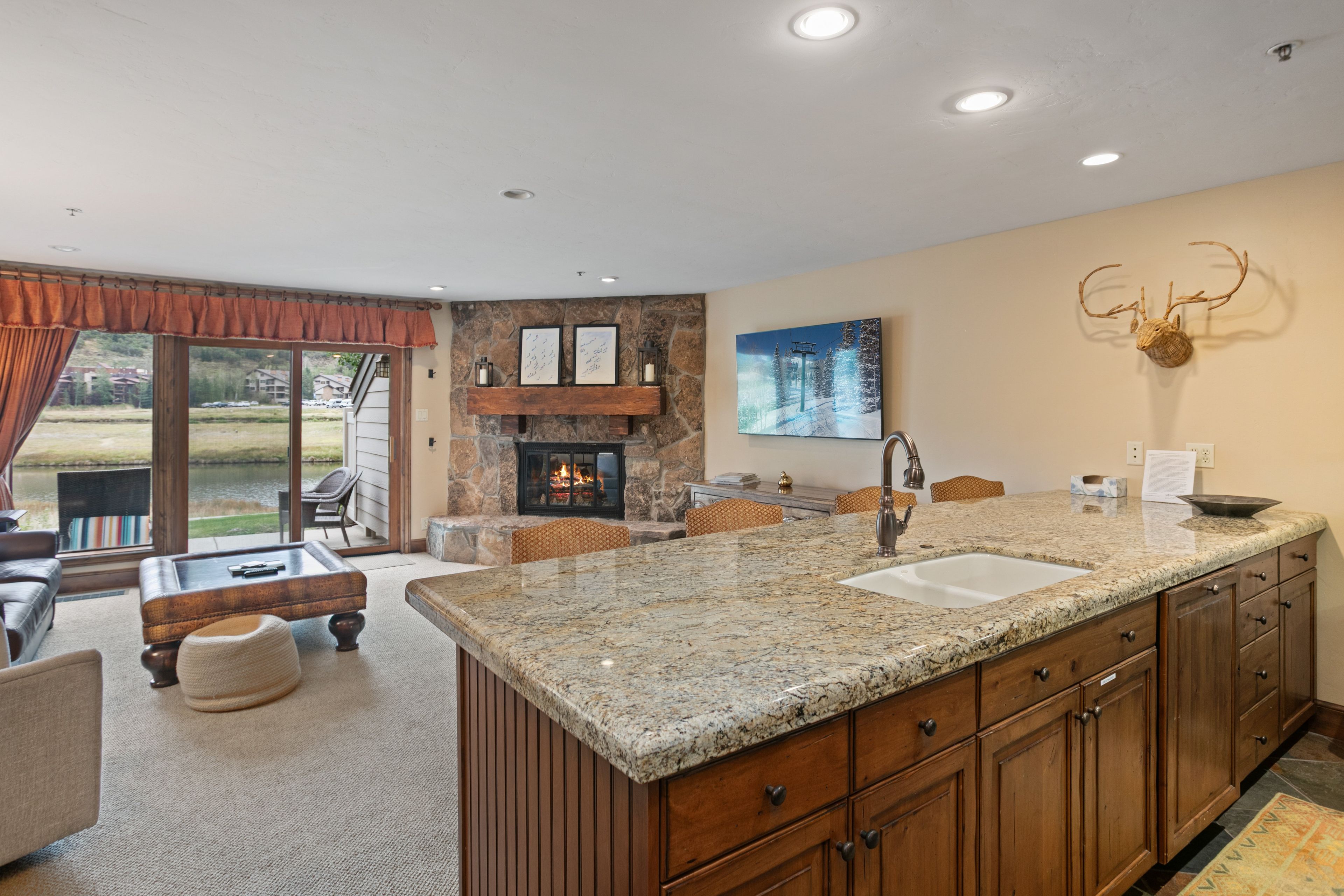 A spacious kitchen with a large granite island, wooden cabinets, and a stone fireplace.
