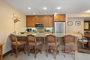 A kitchen with wooden cabinets, a stainless steel refrigerator, a microwave, and a bar area with four wicker chairs. - 2br Deer Valley Retreat Hot Tub & Fireplace 2 Bedroom Condo (Park City)