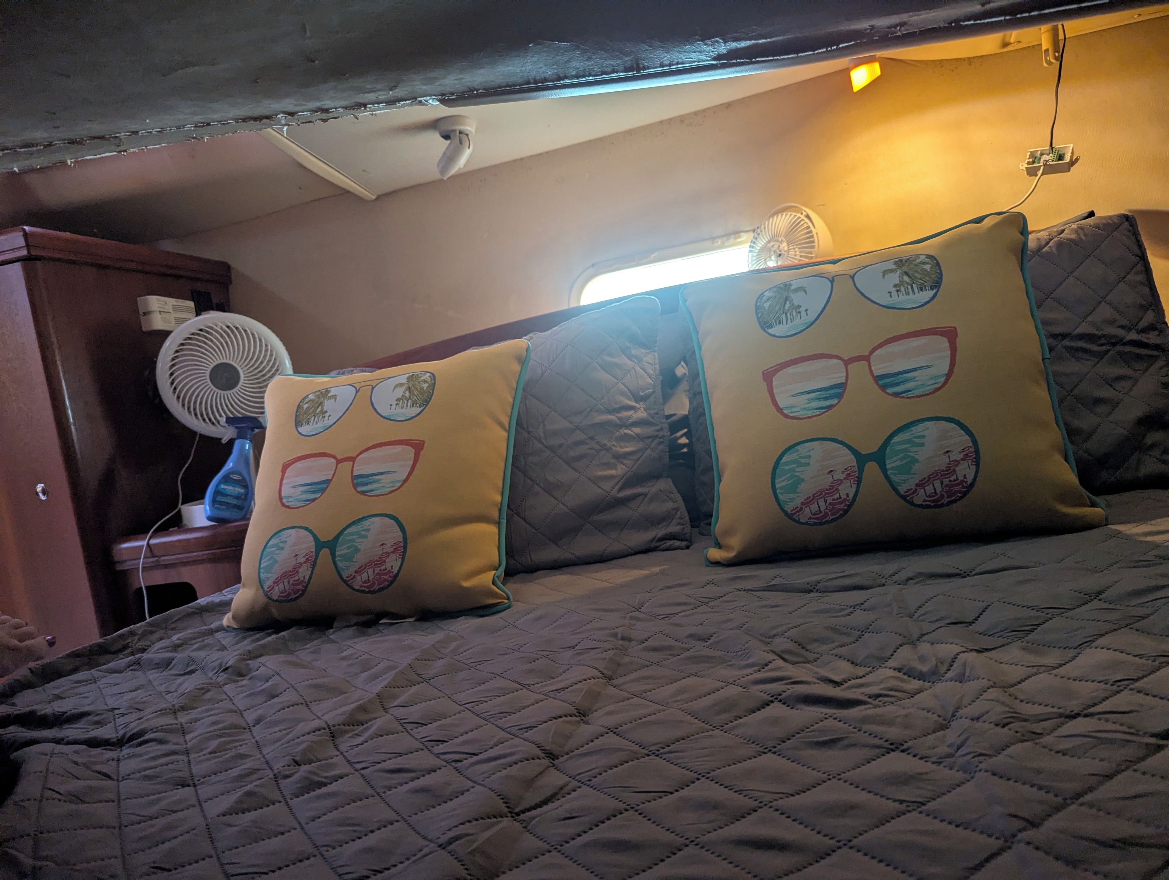 A bed with a quilted cover, two pillows with circular designs, a standing fan, and a wall-mounted light fixture.