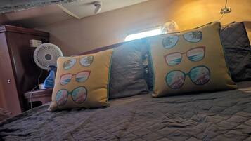 A bed with a quilted cover, two pillows with circular designs, a standing fan, and a wall-mounted light fixture.