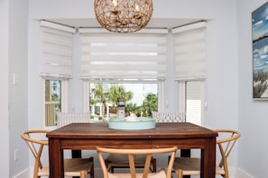 A dining area with a wooden table and chairs, a hanging light fixture, and a view of the outdoors through large windows. - 🌴Sea Cliff A6 | Steps to Beach | Pool | Pet Friendly🌴 (Cape San Blas)