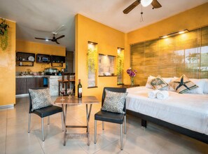 A modern hotel room with a bed, two chairs, a dining table, a kitchen area, and a ceiling fan. - Memory Foam King Bed, Kitchen, AC, Free Coffee, 2 Blue Flag Beaches 10 Min (Playa del Carmen)