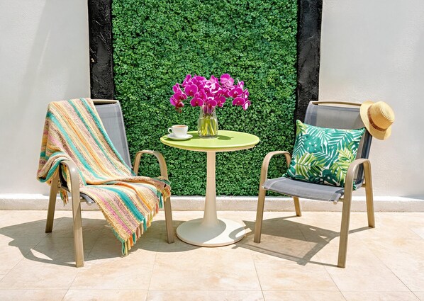 Two chairs with a table between them, a green wall with foliage, and a straw hat on one of the chairs. - Queen and Double Beds Sleep 4, Full Kitchen, AC, 2 Blue Flag Beaches 10 Min Walk (Playa del Carmen)