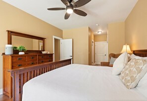 A hotel room with a bed, a dresser, a mirror, a ceiling fan, and a door. - Tropical Oasis at Regency 514 - Steps from Poipu Beach (Koloa)