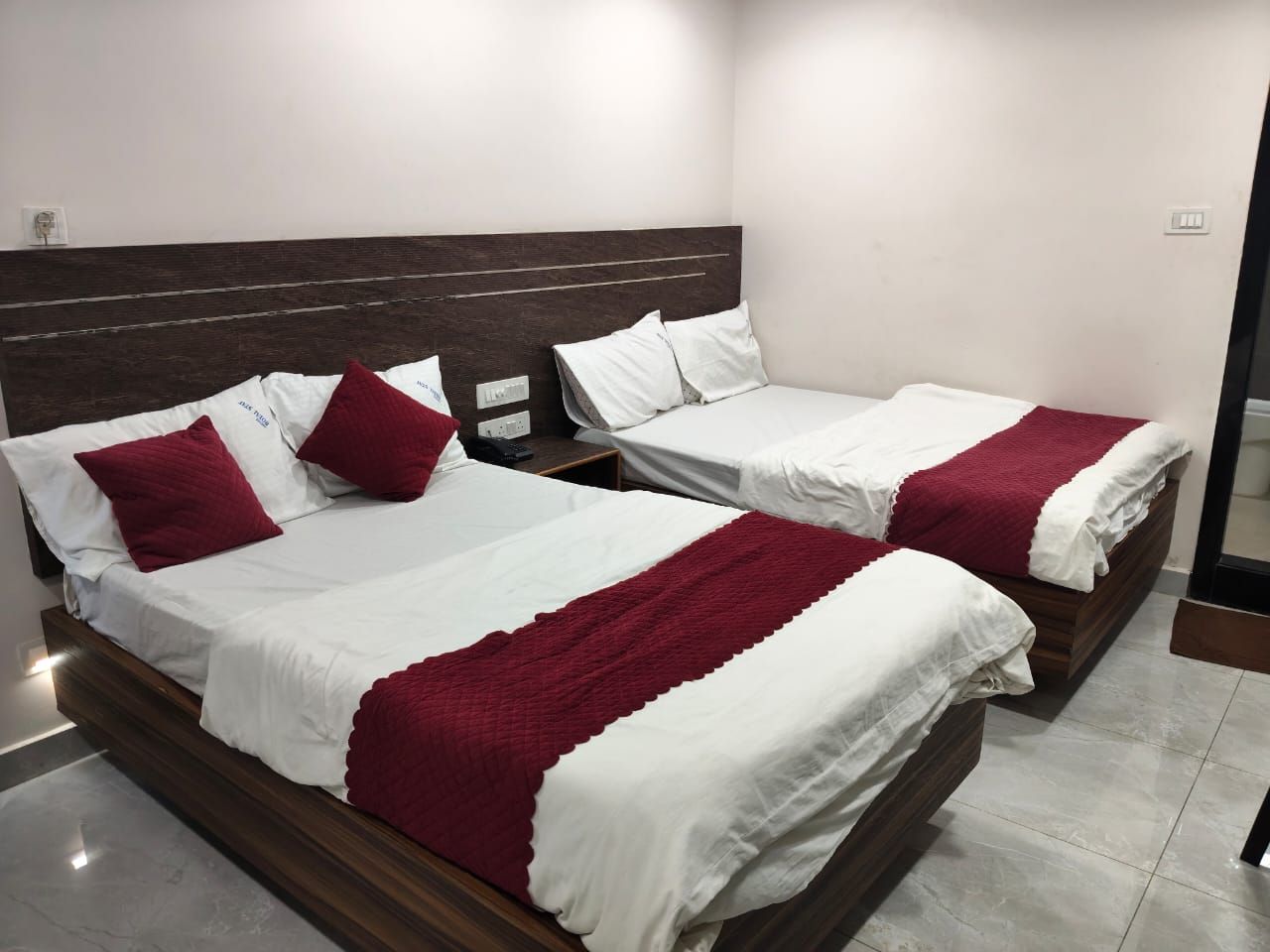 Een hotelkamer met twee bedden, elk met witte beddengoed en rode accenten, en een donker houten hoofdbord.