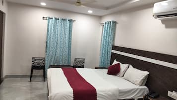 Una habitación de hotel con cama, dos sillas, mesita de noche, aire acondicionado y cortinas.