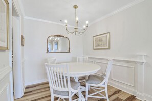 A dining area with a round table, white chairs, a chandelier, a mirror, and a framed picture on the wall. - One bedroom oasis in the heart of sea pines with harbour and lighthouse views (Hilton Head Island)