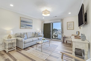 A living room with a sofa, coffee table, and a view through a sliding glass door. - One bedroom oasis in the heart of sea pines with harbour and lighthouse views (Hilton Head Island)