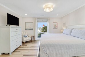 Un dormitorio con cama, televisión, cómoda y vistas a un faro por la ventana.