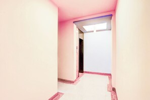 A narrow hallway with a pink wall and a white door at the end. - Townhouse TIPSYY INN 023 (Jaipur)
