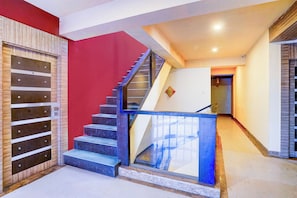 A staircase with a glass railing, a red wall, and a wooden panel on the left. - Townhouse TIPSYY INN 023 (Jaipur)