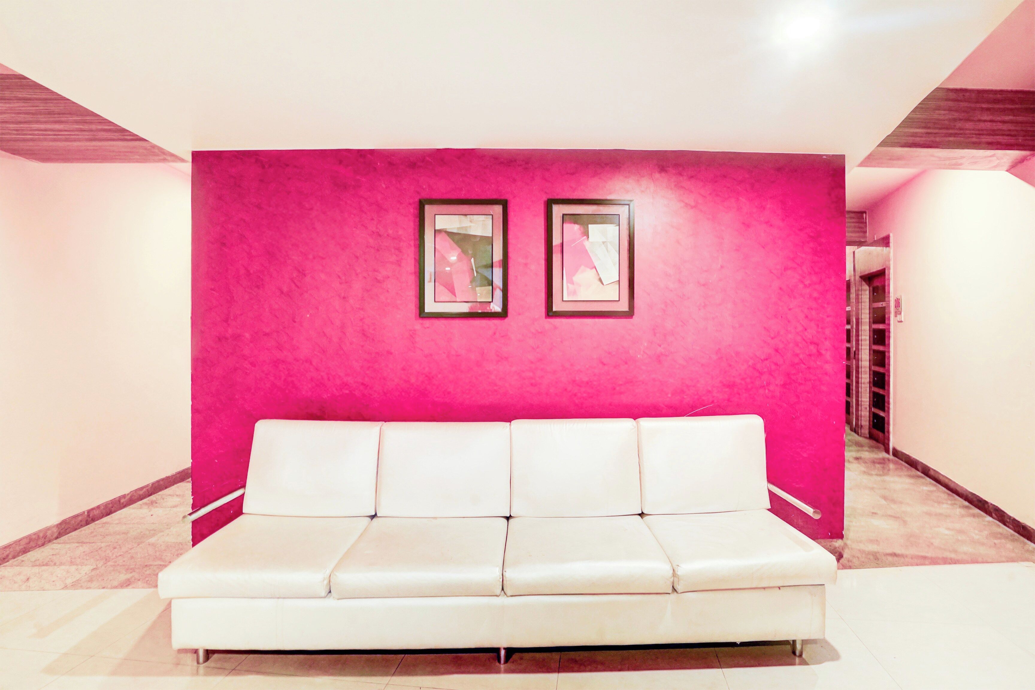 Un sofá blanco en un pasillo con una pared rosa brillante y dos cuadros enmarcados.