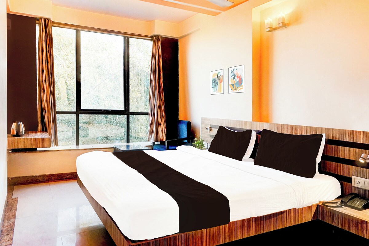 A hotel room with a large bed, a bedside table with a phone, and a window with curtains.