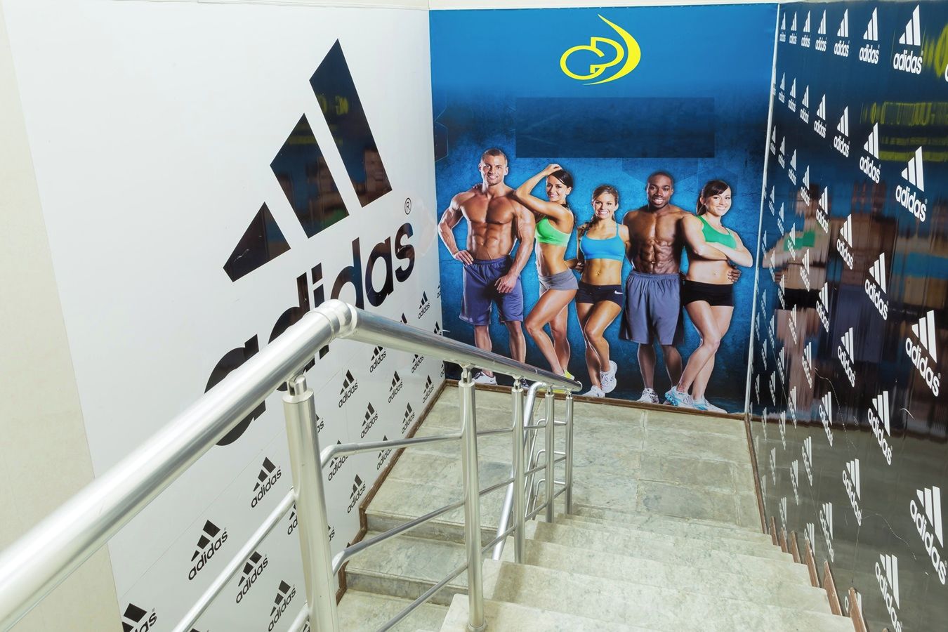 Una escalera con barandillas metálicas y una pared con un gran logotipo de Adidas y un grupo de personas.