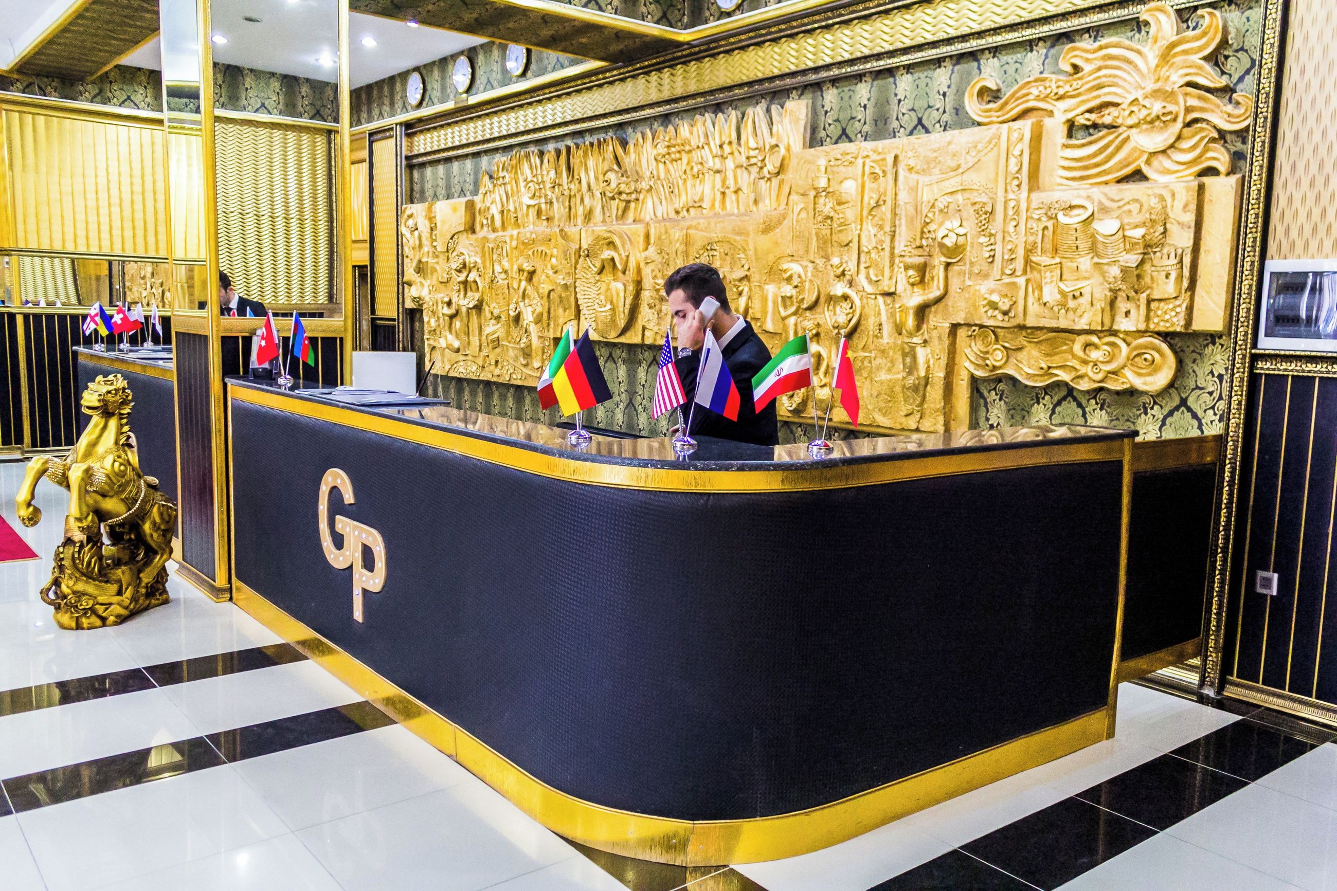 Una mesa de recepción con un logotipo 'GP', varias banderas nacionales y una pared decorativa dorada.