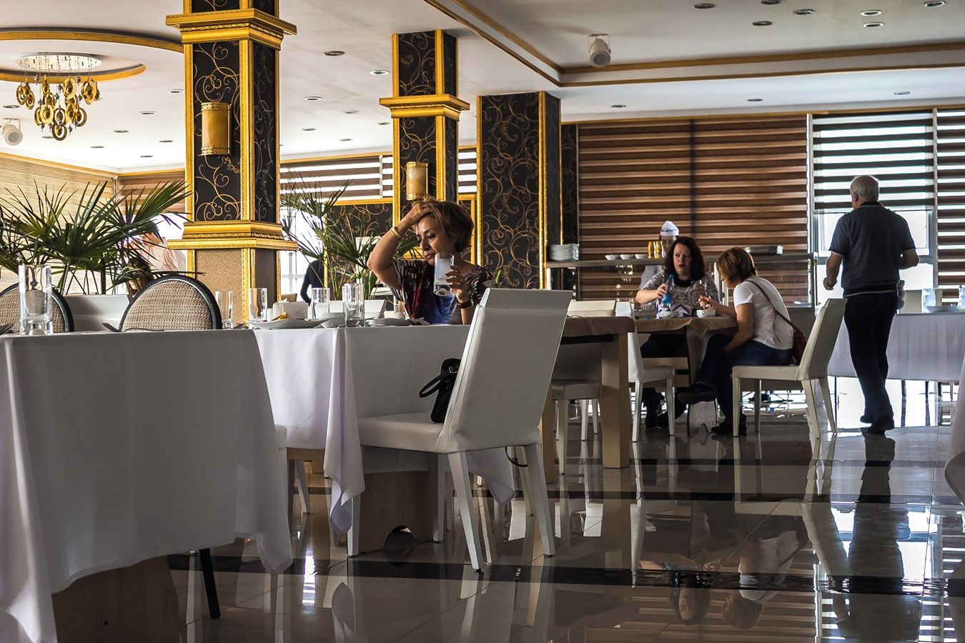 Een restaurant met gedekte tafels, een ober die gasten bedient, en een man die langskomt.