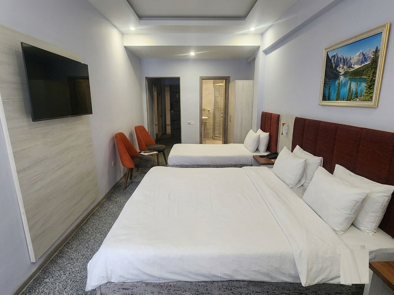 A hotel room with a large bed, a TV mounted on the wall, a painting, and a door leading to another room.