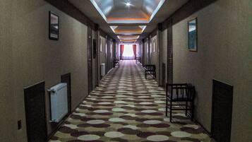 Un pasillo de hotel con alfombra estampada, iluminación empotrada y sillas a lo largo de las paredes.