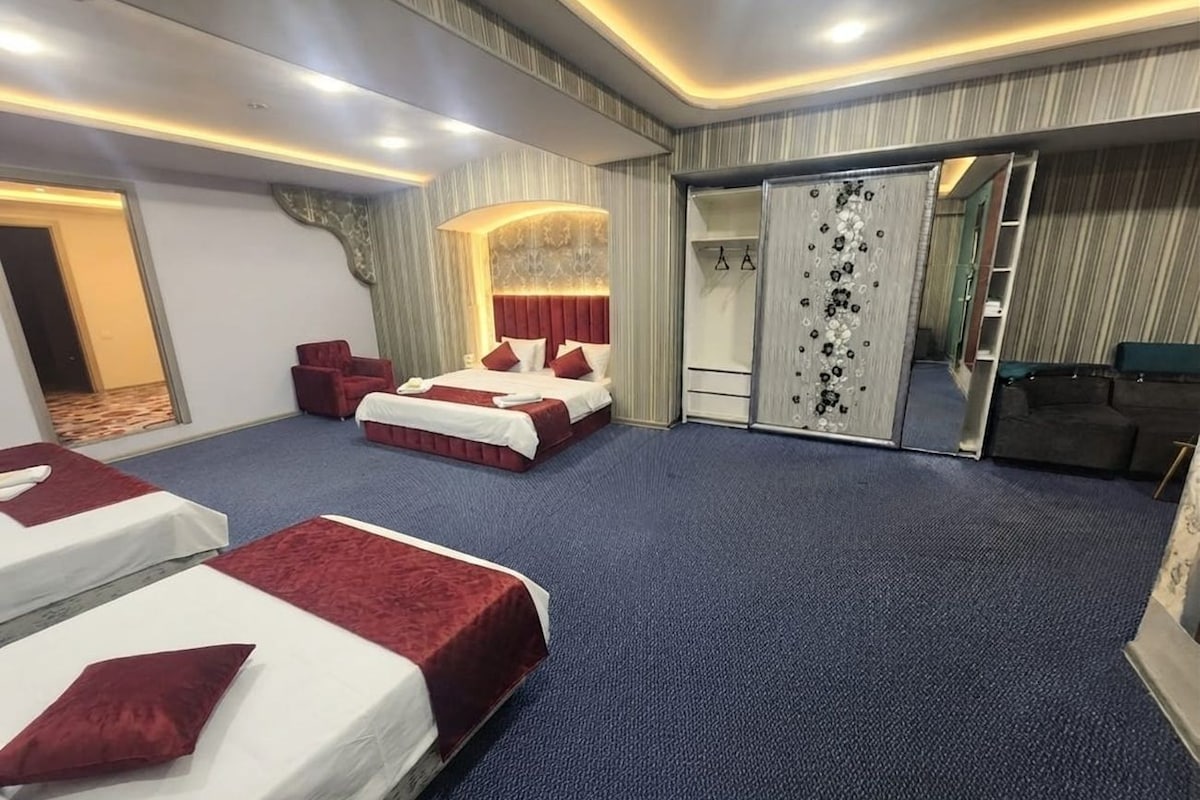 A hotel room with two beds, a sitting area, a wardrobe, and a mirror.