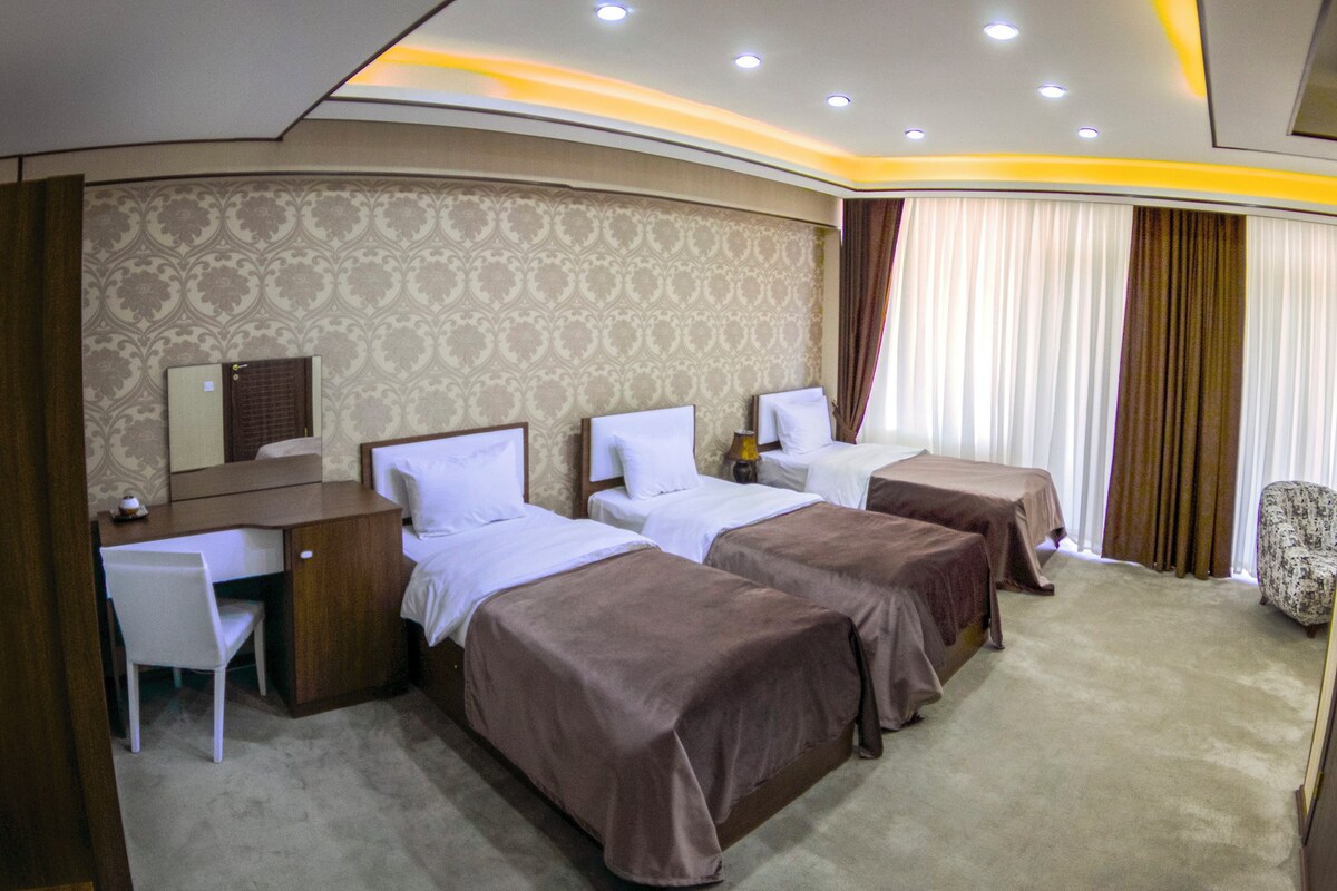 A hotel room with three beds, a desk, a chair, and a mirror.