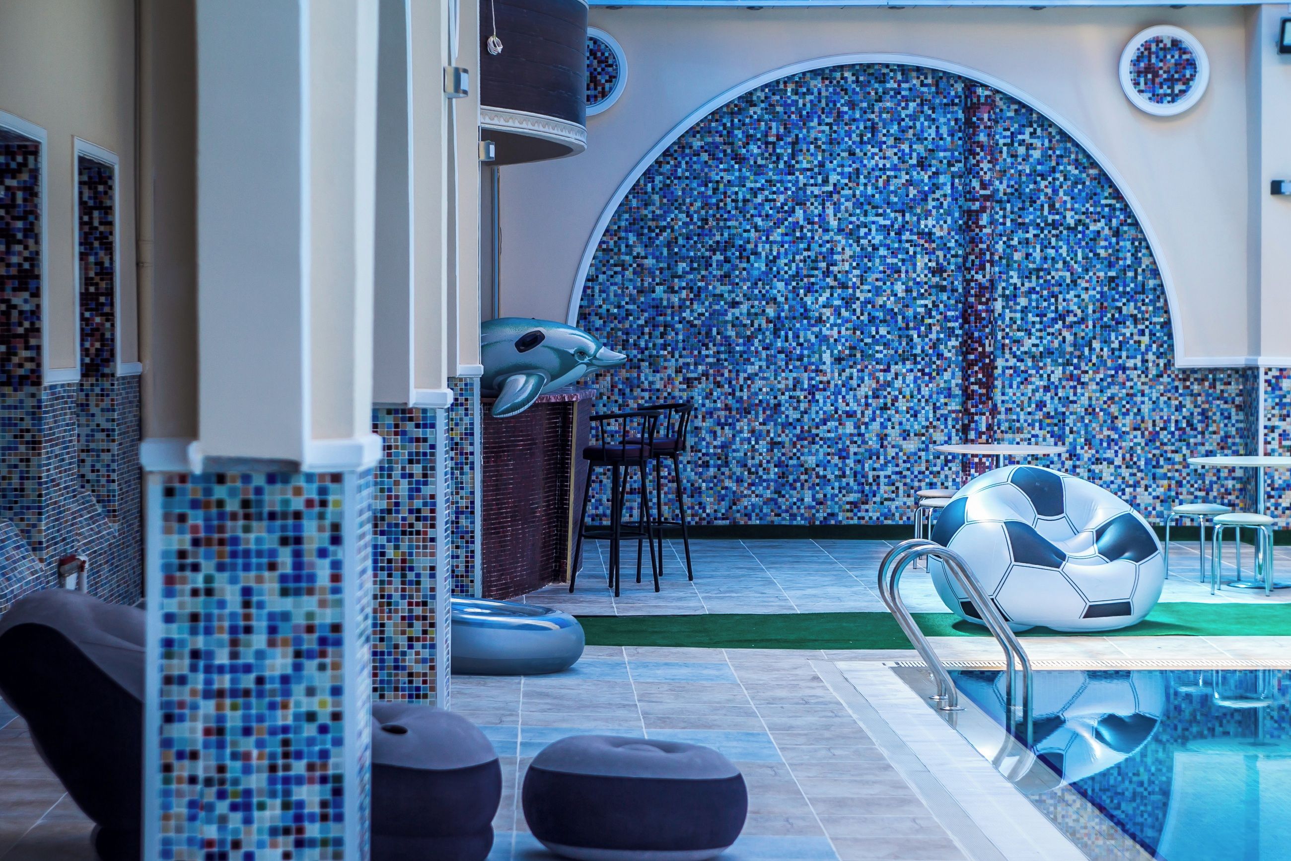 A swimming pool area with a mosaic wall, seating, and a soccer ball decoration.