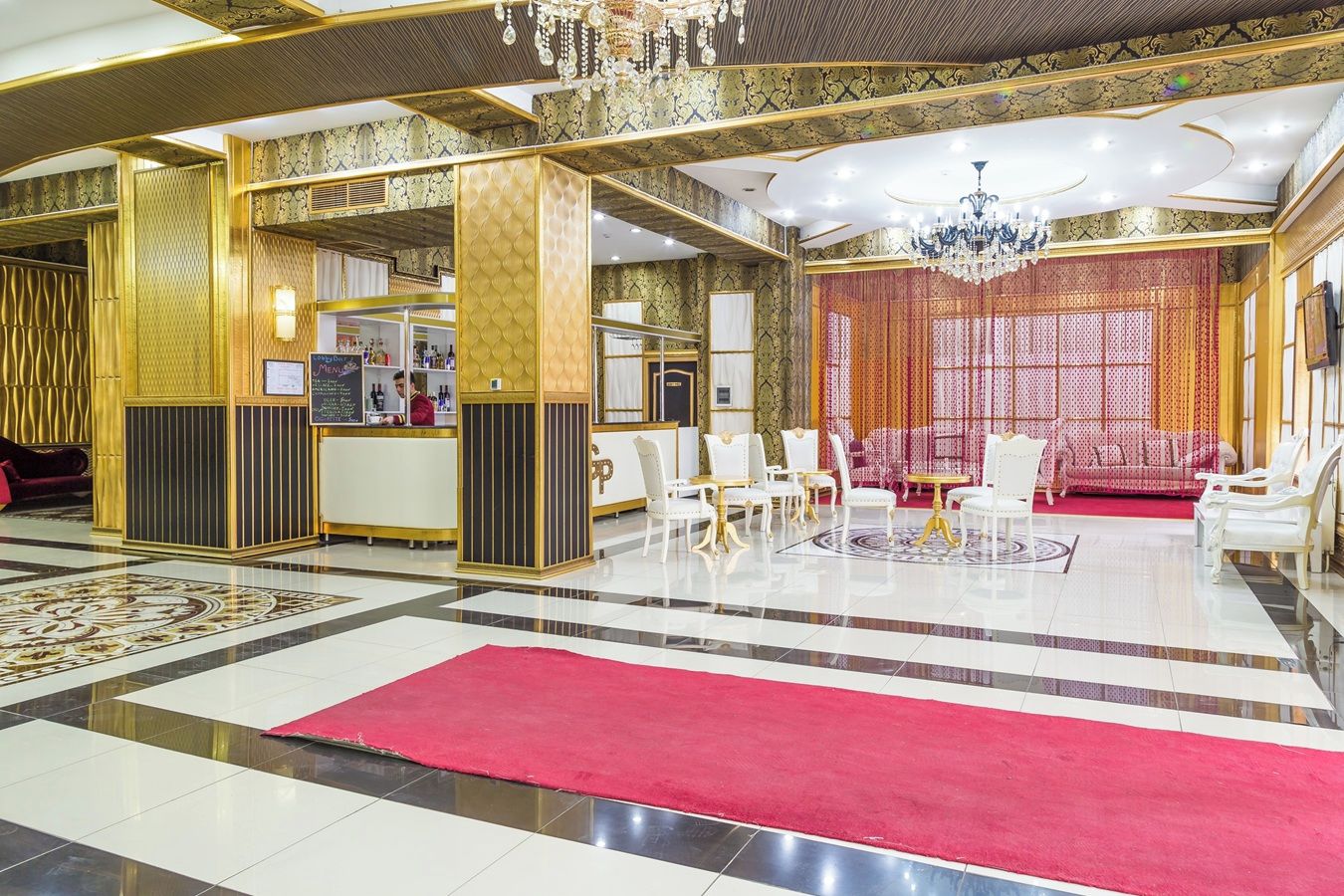 Un lobby lujoso con alfombra roja, sillas blancas y una zona de bar.