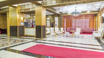 Un lobby lujoso con alfombra roja, sillas blancas y una zona de bar.