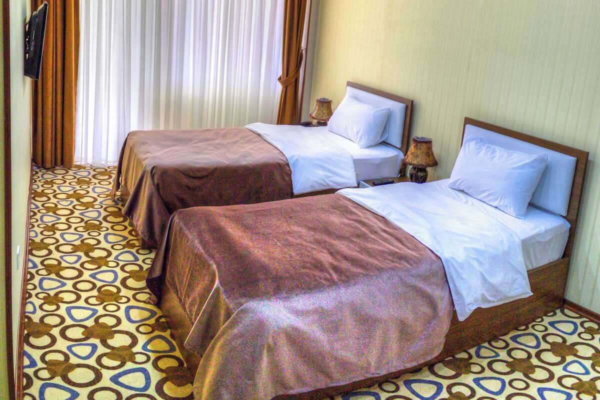 A hotel room with two beds, a patterned floor, and a large window with curtains.